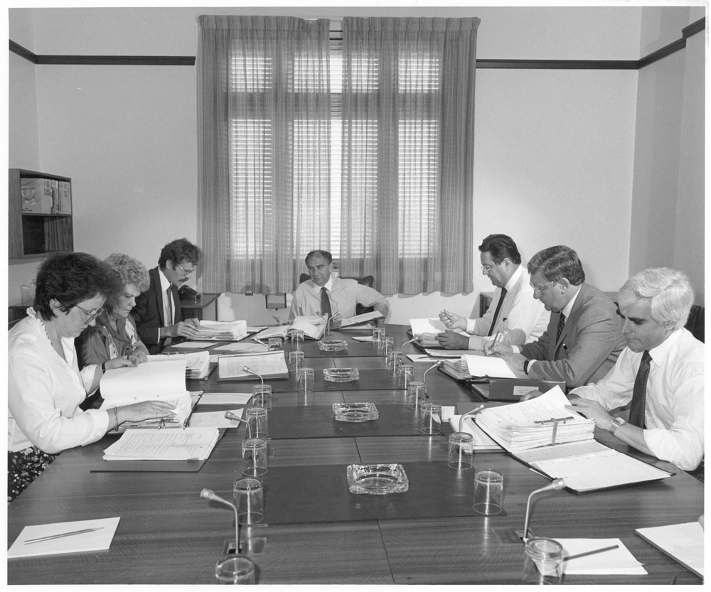 Standing Committee on Regulations and Ordinances in session, 31 March 1987. L-R: Senators Amanda Vanstone and Patricia Giles, Peter Oâ€™Keeffe [Secretary], Senators Barney Cooney [Chair], Reg Withers, Austin Lewis [Deputy Chair] and John Coates. NAA: A6180, 31/3/87/63.